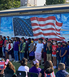 Students standing in from of mural of American flag